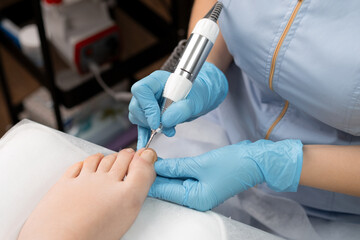 A pedicure expert in rubber gloves, performs a hardware pedicure for woman, utilizing a nail drill.