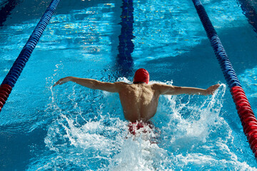 Athleticism in action. Young muscular man, swimmer in motion, action, training, swimming in pool...