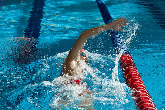 Dynamic image of young man, swimmer in cap and goggles in action, motion, swimming freestyle stroke in pool. Concept of professional sport, health, endurance, strength, active lifestyle