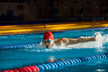 Young muscular man showing competitive spirit, swimmer in cap and goggles training, swimming in...
