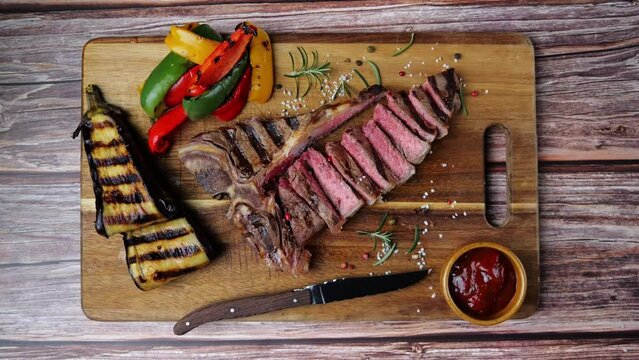 T- bone beef steak grilled sliced with grilled vegetables on wooden board. Top view