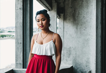 A woman standing in front of a window wearing a white top and a red skirt.