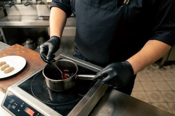close up in a professional kitchen chef in a black jacket mixes the sauce in a saucepan