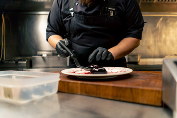 in professional kitchen with a chef in black gloves laying out dessert on a plate