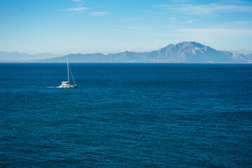 sailboat sailing the waters of the Alboran Sea, with the mountains of the African continent in the...