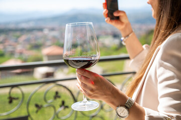 A girl holds a glass of wine against the backdrop of a spring vineyard and takes a selfie....