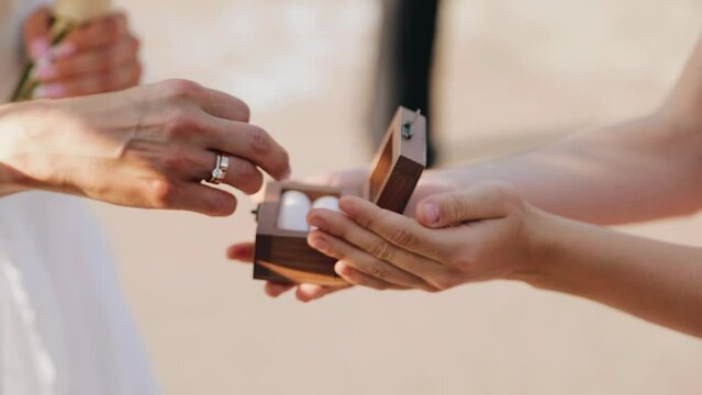 A girl takes an engagement ring from a jewelry box to put it on her man's hand.