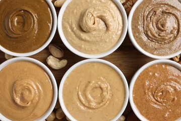 Many tasty nut butters in bowls and nuts on wooden table, flat lay