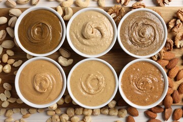 Many tasty nut butters in bowls and nuts on white table, flat lay
