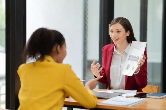 Two businesswomen are actively discussing financial charts and project data during an engaging office meeting, collaborating on strategy and sharing insights - Powered by Adobe