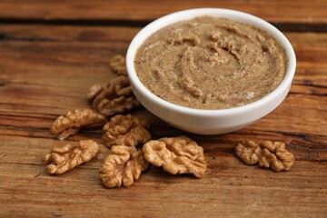 Delicious nut butter in bowl and walnuts on wooden table, closeup