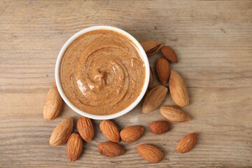 Delicious nut butter in bowl and almonds on wooden table, top view
