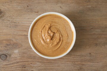 Delicious nut butter in bowl on wooden table, top view