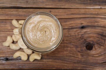 Tasty cashew nut paste in jar on wooden table, top view. Space for text