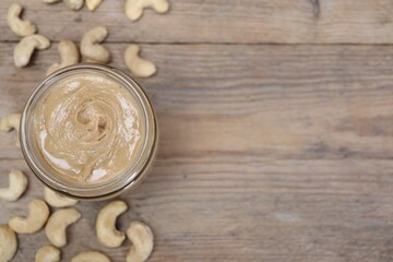 Tasty cashew nut paste in jar on wooden table, top view. Space for text