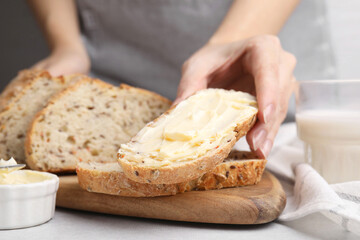 Woman taking slice of bread with tasty butter at table, closeup