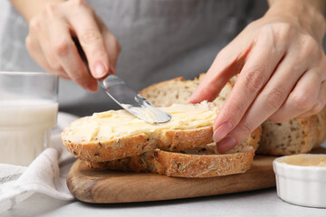 Woman spreading tasty butter onto bread at table, closeup