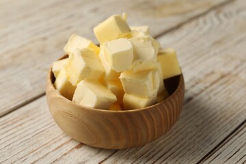 Tasty butter cubes in bowl on light wooden table