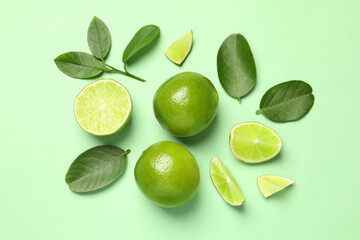 Fototapeta premium Whole and cut fresh ripe limes with leaves on light green background, flat lay