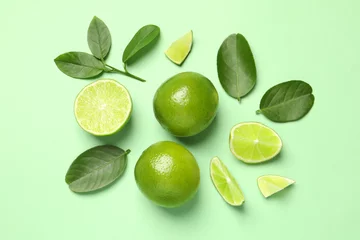 Foto auf Leinwand Whole and cut fresh ripe limes with leaves on light green background, flat lay © New Africa