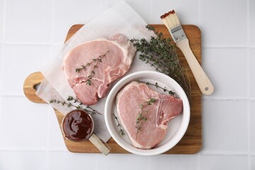 Raw meat, thyme, basting brush and marinade on white tiled table, top view