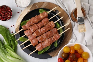 Wooden skewers with cut raw marinated meat on white tiled table, flat lay