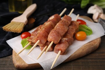 Skewers with cut raw marinated meat on wooden table