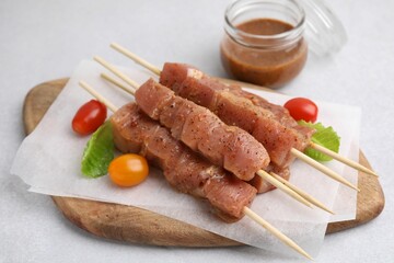 Wooden skewers with cut raw marinated meat on light grey table