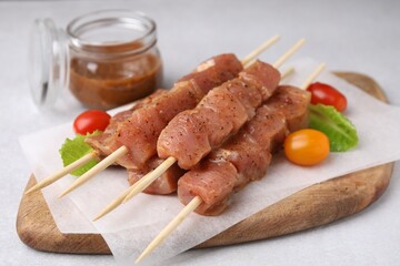 Wooden skewers with cut raw marinated meat on light grey table, closeup