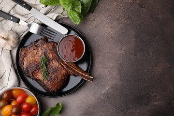 Tasty grilled meat, rosemary and marinade served on brown textured table, flat lay. Space for text