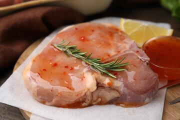 Board with raw marinated meat and rosemary on wooden table, closeup