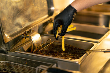 close-up in a professional kitchen a chef in black gloves puts French fries into a deep fryer