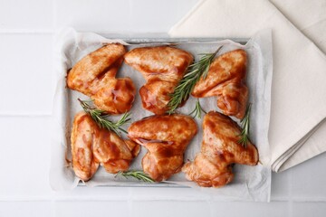 Raw marinated chicken wings and rosemary on light tiled table, top view