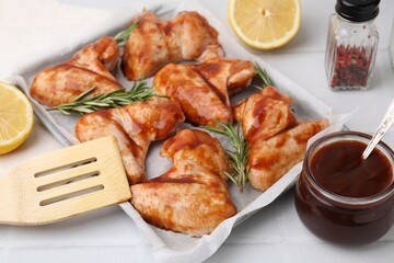 Raw marinated chicken wings, rosemary and spatula on light tiled table, closeup