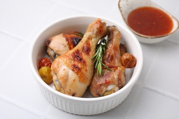 Marinade, roasted chicken drumsticks, rosemary and tomatoes on white tiled table, closeup