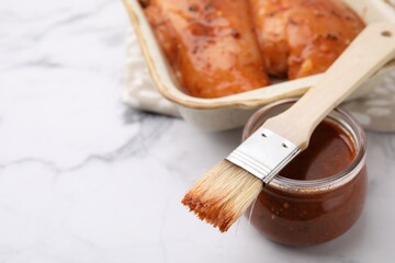 Fresh marinade, basting brush and raw chicken fillets on white table, closeup. Space for text