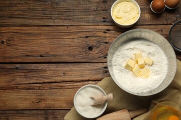 Flat lay composition with fresh butter and flour in bowl among other products on wooden table....