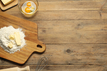 Board with fresh butter and flour on wooden table, flat lay. Space for text