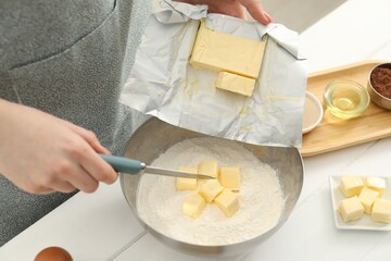 Woman adding fresh butter into bowl with flour at white wooden table, closeup