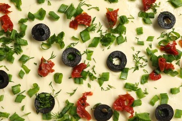 Fresh natural butter with cut olives, onion and sun-dried tomatoes as background, top view