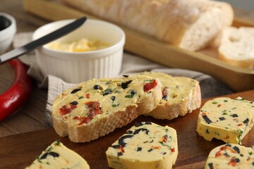 Tasty butter with olives, chili pepper, parsley and bread on wooden table, closeup
