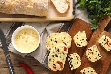 Tasty butter with olives, chili pepper, parsley and bread on wooden table, top view