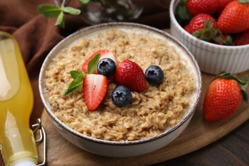 Tasty oatmeal with strawberries and blueberries in bowl on wooden table, closeup