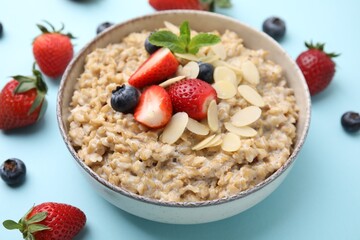 Tasty oatmeal with strawberries, blueberries and almond flakes in bowl on light blue background, closeup