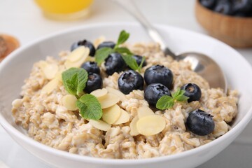 Tasty oatmeal with blueberries, mint and almond petals in bowl on white table, closeup