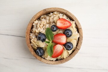 Tasty oatmeal with strawberries, blueberries and almond petals in bowl on white wooden table, top view
