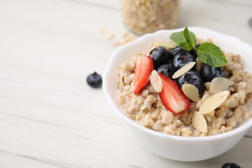 Tasty oatmeal with strawberries, blueberries and almond petals in bowl on white wooden table, closeup. Space for text