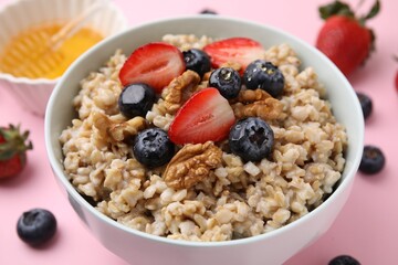 Tasty oatmeal with strawberries, blueberries and walnuts in bowl surrounded by fresh berries on pink background, closeup