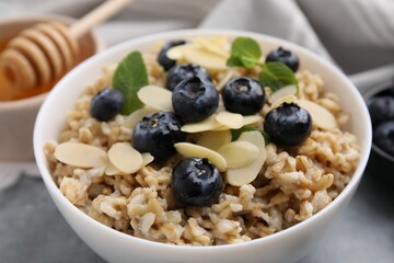 Tasty oatmeal with blueberries, mint and almond petals in bowl on grey table, closeup