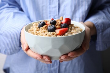 Woman holding bowl of tasty oatmeal with strawberries, blueberries and walnuts, closeup